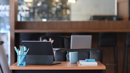 Front view of contemporary workplace with a tablet computer, coffee cup, notebook and stationery on wooden desk.