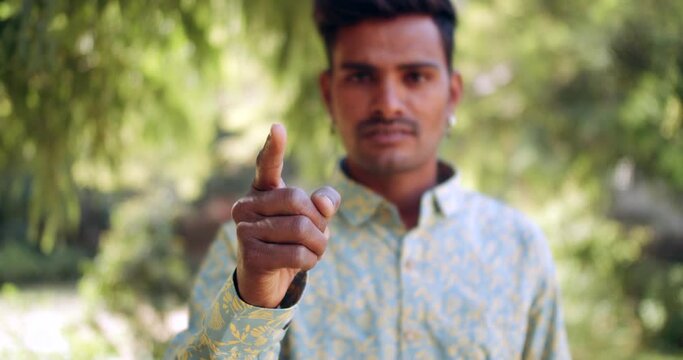 Slow-motion static close-up portrait of a young adult Indian man outdoors in sign gesture pointing finger straight at camera with stare and warning angry - blurred defocused racking focus shift 