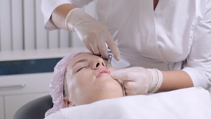 Fototapeta premium Beautician doctor makes injections into the skin of the face of an adult woman. Cosmetic injection with hyaluronic acid. Concept of mesotherapy, biorevitalization, cosmetology. 