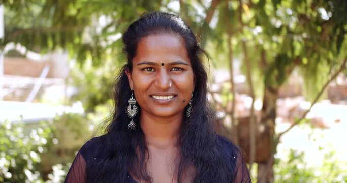 Slow-motion close-up portrait of a young beautiful adult Indian woman outdoors smiling as she thinks deliberates and speaks and listens to someone off camera 