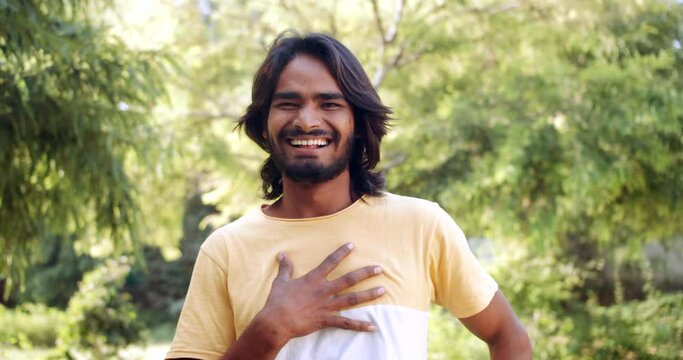 Slow-motion close-up portrait of a young beautiful adult Indian man outdoors laughing joke funny hilarious cant stop with long pretty black hair to groom in nature park trees green 