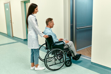 Young beautiful woman doctor with her disabled elderly patient in a wheelchair approached the elevator of a modern hospital. © Valerii Apetroaiei