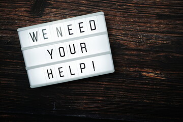 We Need Your Help word text in light box on wooden background