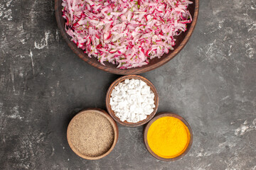 Above view of vegetable salad with various ingredients in a brown bowl and different spices lined up on dark background