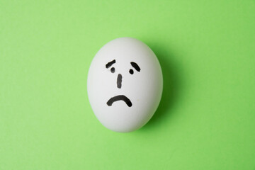 Fototapeta na wymiar Egg with a very sad emotion on the face, on a green background with copy space