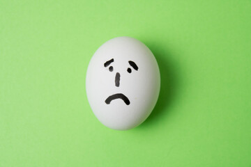 Egg with a very sad emotion on the face, on a green background with copy space