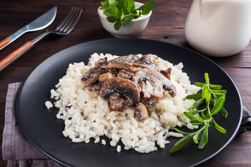 Risotto with mushrooms on a black plate. Boiled white rice with champignons in cream sauce. Dark wooden background. close up
