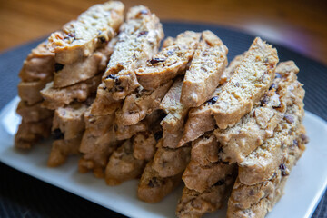 A stack of homemade biscotti on white ceramic plate, sitting on a black woven placemat on a wooden countertop