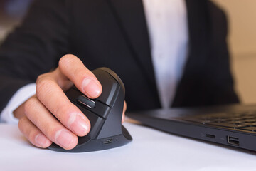 A person working at home in front of a computer holding a computer ergonomic mouse.