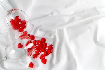 Happy Valentine's Day background - red little hearts lie in an empty glass glass on a white fabric with folds with space for text and flat lay