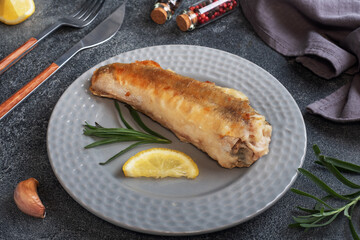 Fried fish hake Pollock and slices of fresh lemon. Dark concrete background. Copy space.