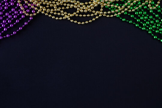 Mardi gras background on black with purple, yellow, green beads copy space