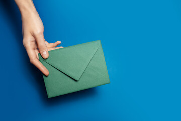 Close-up of female hand holding a green paper envelope on background of blue color.