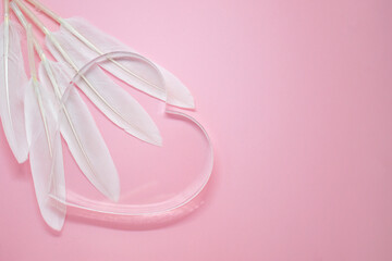 Transparent glass heart and white feathers on pale pink background. Place for your text. Valentine card, declaration of love, postcard, wedding invitation.