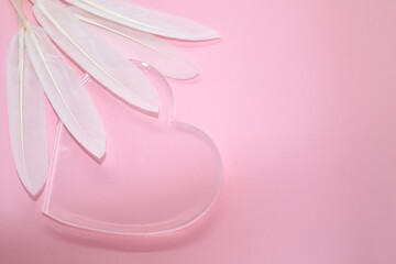 Transparent glass heart and white feathers on pale pink background. Place for your text. Valentine card, declaration of love, postcard, wedding invitation.