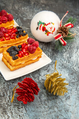 bottom half view berry waffles on white rectangular plate bowls of pomegranate and raspberries and xmas pendants on grey-white background