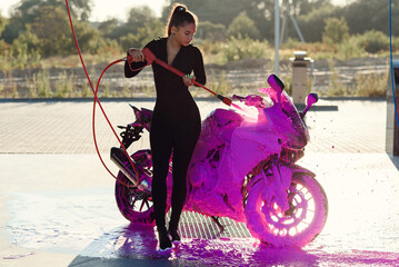 Obraz na płótnie Canvas Beautiful pretty girl in tight-fitting seductive suit washes a motorcycle at self-service car wash service.