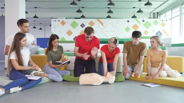 Young male practicing CPR first aid on a mannequin in the presence of people, indoors