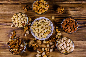 Various nuts (almond, cashew, hazelnut, pistachio, walnut) in bowls on a wooden table. Vegetarian meal. Healthy eating concept. Top view