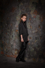 beautiful girl in a large jacket and leather pants posing against the background of an old wall