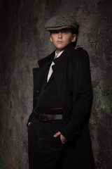 boy teenager in a cap and black coat posing against the background of an old wall