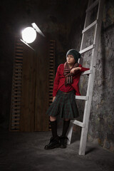 guy teenager by the old wall with a ladder in a knitted hat and tartan skirt