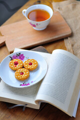 a cup of tea with a book and cake as decor