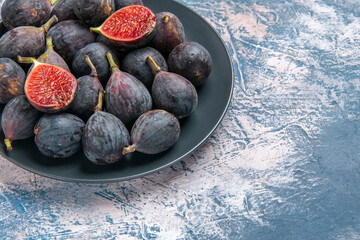 Half shot of full fresh black mission figs split ones on a black plate on red stripped towel on gray table