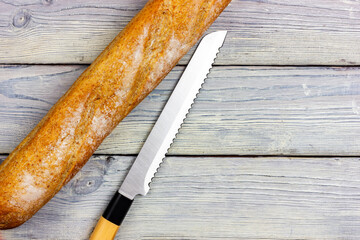 White crispy baguette and bread knife on a light wooden table in Provence style. View from above. Slicing a fresh crispy baguette