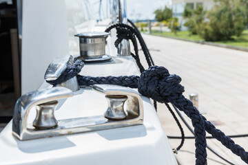 Detail of an anchor rope on a yacht, Stainless steel boat mooring cleat with knotted rope mounted on white yacht deck