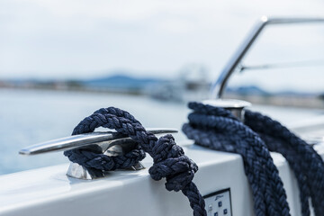 Detail of an anchor rope on a yacht, Stainless steel boat mooring cleat with knotted rope mounted on white yacht deck - Powered by Adobe
