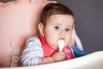 Baby is smeared with porridge, eats and looks into the camera.