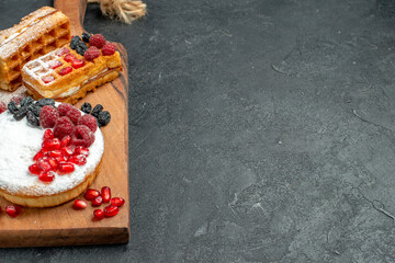 bottom close view tart and waffles with berries on wood cutting board on dark background with copy space