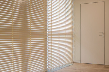 Fototapeta na wymiar Motorized wood blinds in the interior. Automatic venetian blinds beige color on large windows. Coulisse wooden slats 50mm wide. A door to the room is near the window. 