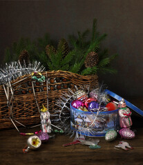 Old glass Christmas decorations and fir branches in a basket on a dark wooden table.