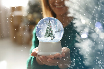 Woman holding snow globe with Christmas tree at home, focus on hands