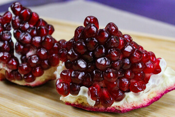 Two pieces of pomegranate with red seeds on a wooden tray. Pomegranate seeds. One piece in front...