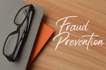 Top view of eyeglasses, notebooks over wooden background written with text FRAUD PREVENTION....