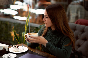 young brunette woman drinking coffee in a cafe and eating dessert
