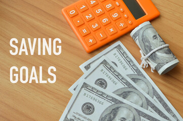 Selective focus of money banknotes and calculator over wooden background written with text SAVING...