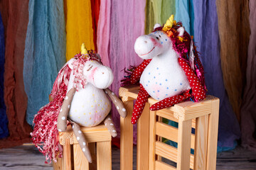 Two textile toys unicorns sitting on wooden box. Close-up.