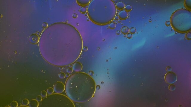 Abstract drops, bubbles and spheres of oil on water, macro photography. Dark glowing blue background.