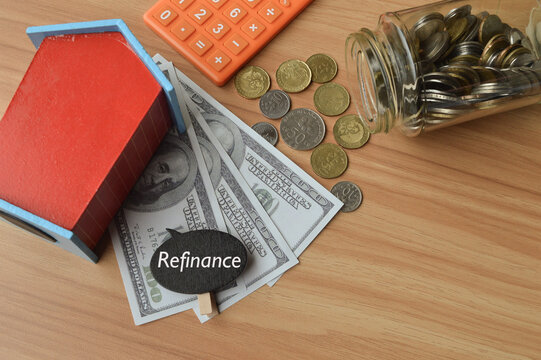 Top angle view of toy wooden house, money banknotes, calculator, coins and wooden tag written with REFINANCE over wooden background. Business concept.