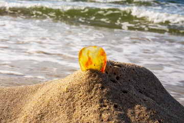 Amber on a sandy beach. One piece of transparent mineral Sunstone on the background of the sea. Ancient resin, processed amber on a sandy beach, blurred background of sea waves in the background. 