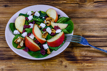 Salad with spinach leaves, feta cheese, cranberries, walnuts and apple in a ceramic plate