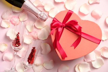 Heart shaped box, champagne bottle and glasses on pink table with rose petals. Valentine's day, Mother's day, anniversary concept. Flat lay, top view.