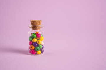 Colored wooden beads in a glass bottle on purple background. DIY folk necklace. Vial with multicolored balls of bead
