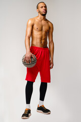 Fototapeta premium Muscular african american sportsman playing basketball shitless over light grey background