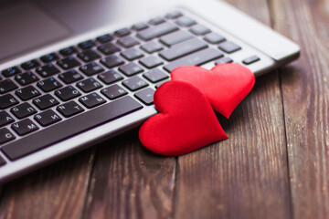 Two red hearts lie on a wooden table near a laptop, Valentine's day wedding love