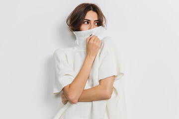 Hiding. Portrait of beautiful brunette woman in comfortable soft longsleeve isolated on white studio background. Home comfort, emotions, facial expression, winter mood concept. Copyspace.